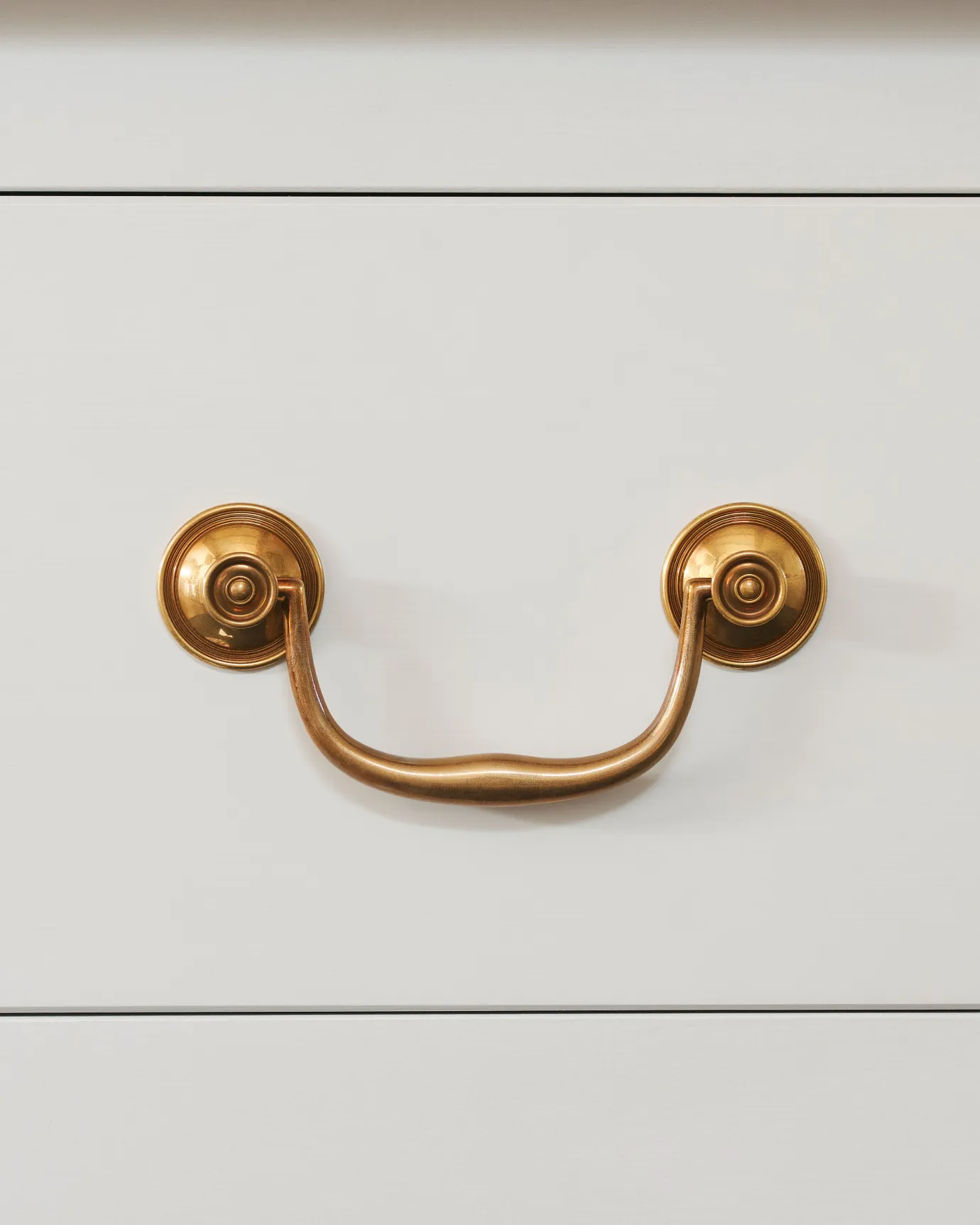 A front-on view of an elegant Georgian-style brass swing handle for kitchen cupboard drawers.