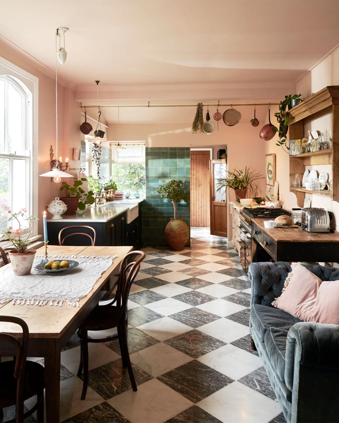 An eclectic kitchen with peach coloured walls, vintage furniture and styling, glossy teal wall tiles and a black and white chequered marble floor.