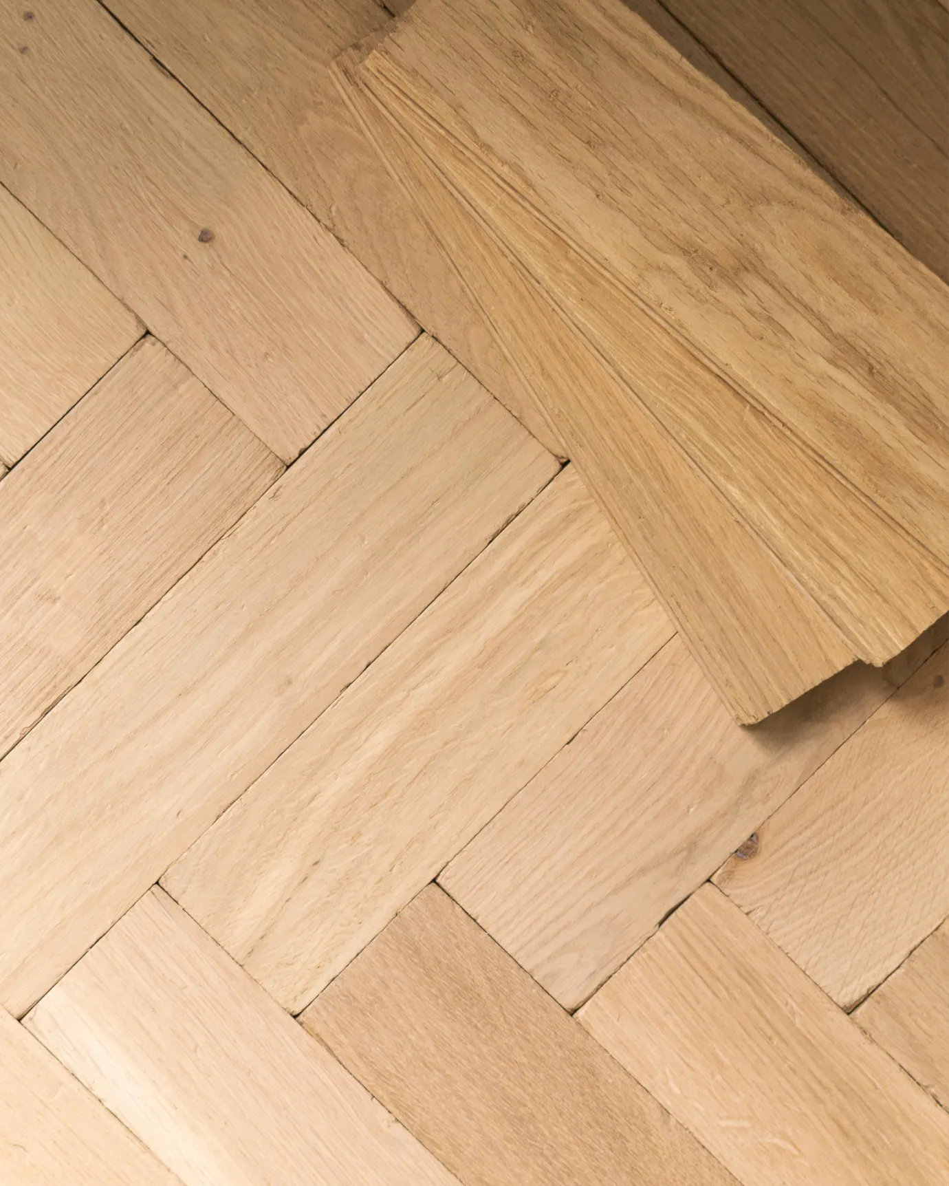 A close-up overhead view of oak parquet flooring with a light natural finish. Three loose blocks are stacked in one corner.