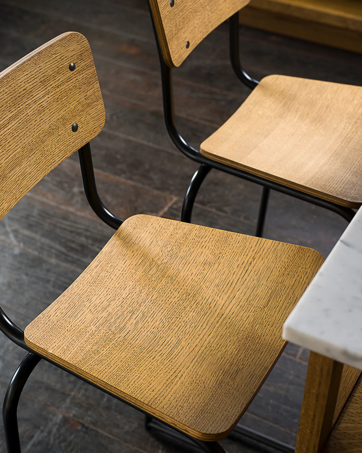 A close-up view of two industrial bar stools with oak veneer plywood seat pans and backrests.