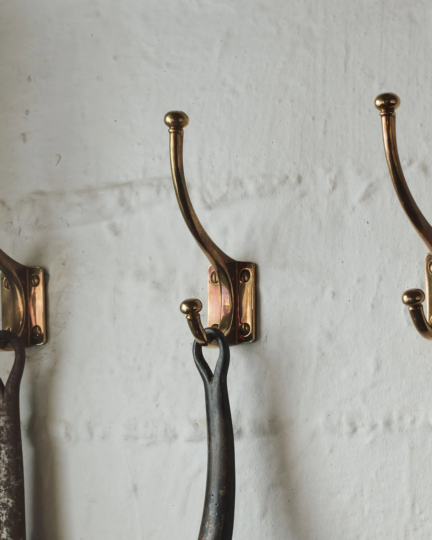 An Edwardian-style brass hook, fitted to a white painted wall.